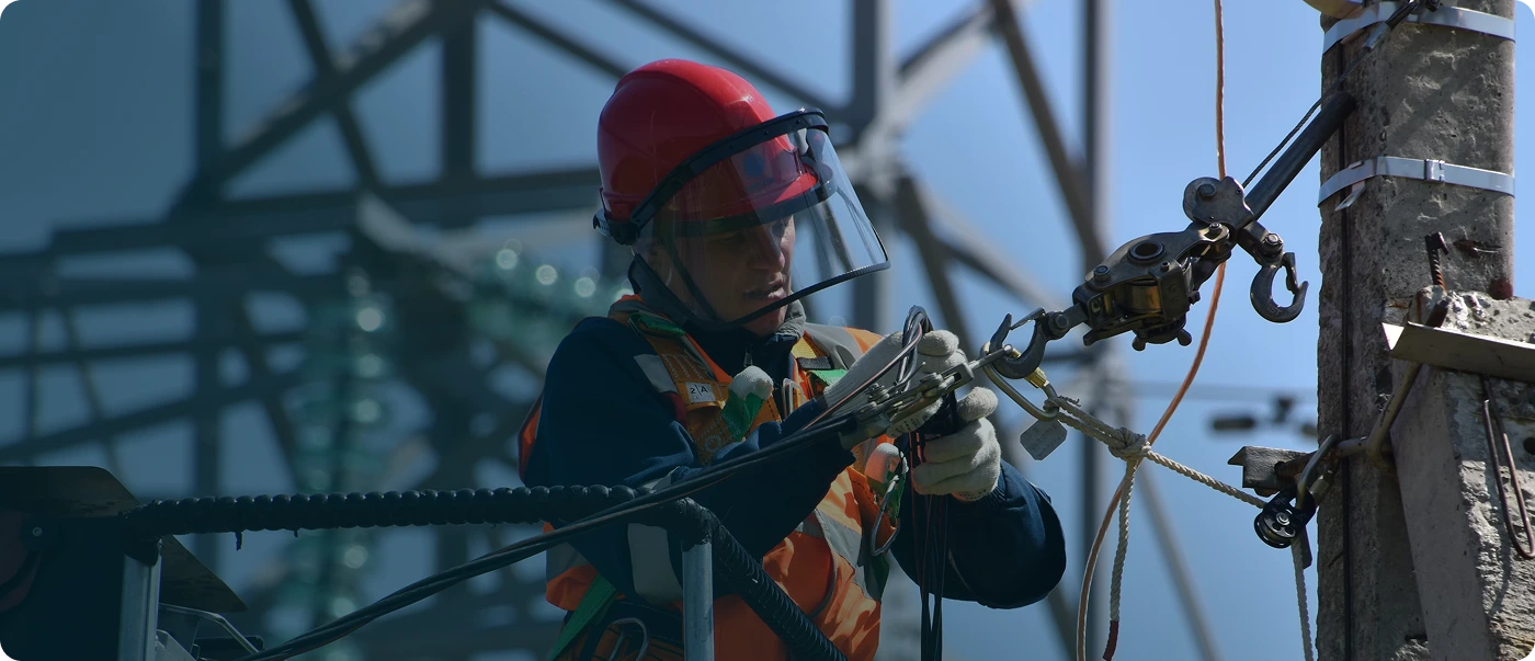 Электромонтажник в защитном шлеме и спецснаряжении работает на высоте на линии электропередач.